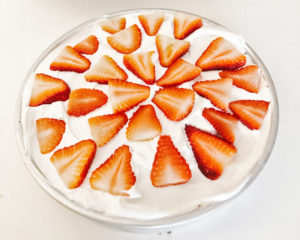 Red Velvet Dr. Pepper Cake topped with whip cream and sliced strawberries