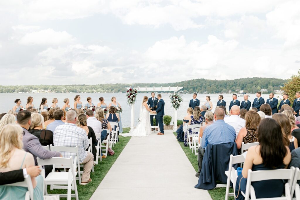 Ceremony at Bay Pointe Inn Pavilion during Mackenzie & Russell’s Shelbyville Michigan wedding with sunset over Gun Lake