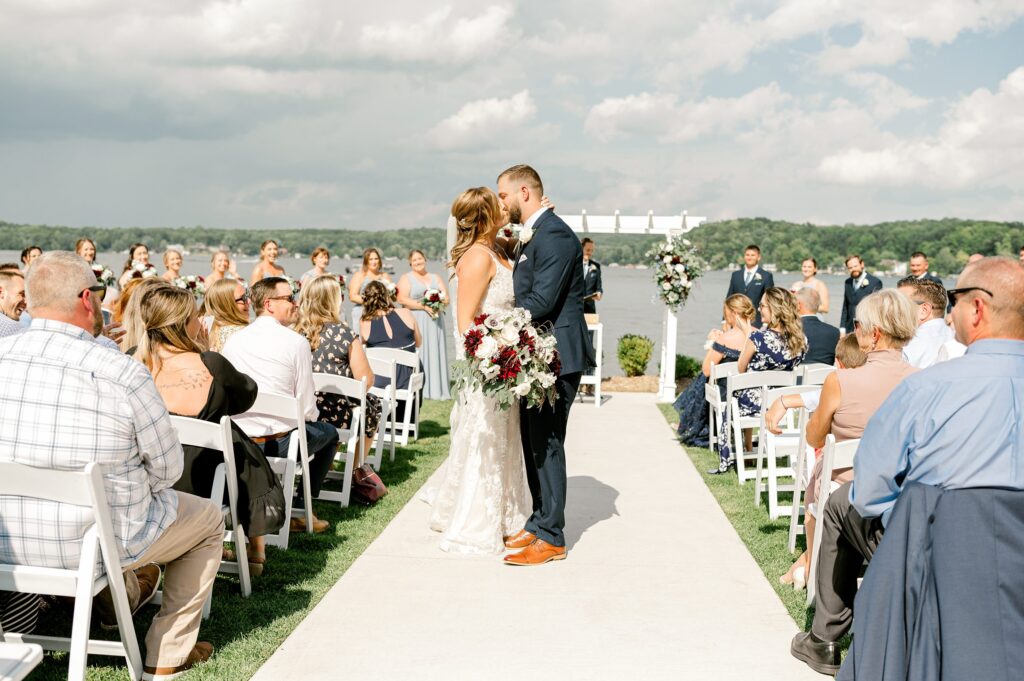 Ceremony at Bay Pointe Inn Pavilion during Mackenzie & Russell’s Shelbyville Michigan wedding with sunset over Gun Lake