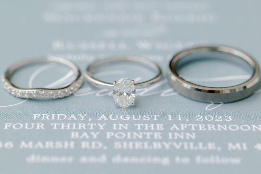 Wedding details including rings, flowers, and invitations at Mackenzie & Russell’s Shelbyville Michigan Bay Pointe Inn wedding
