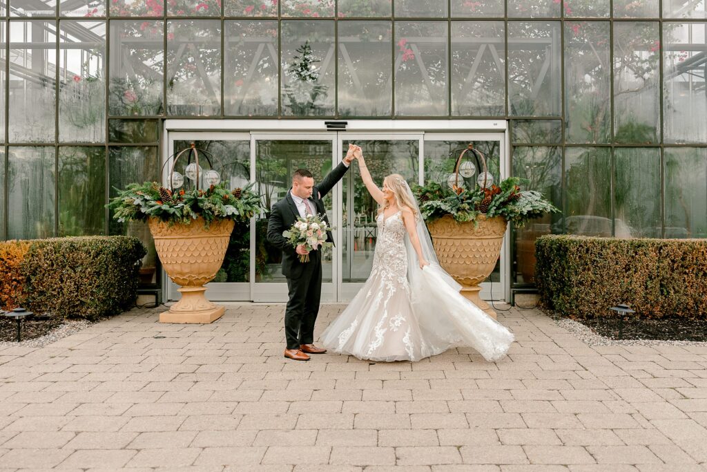 groom twirls bride around in front of greenhouse wedding venue