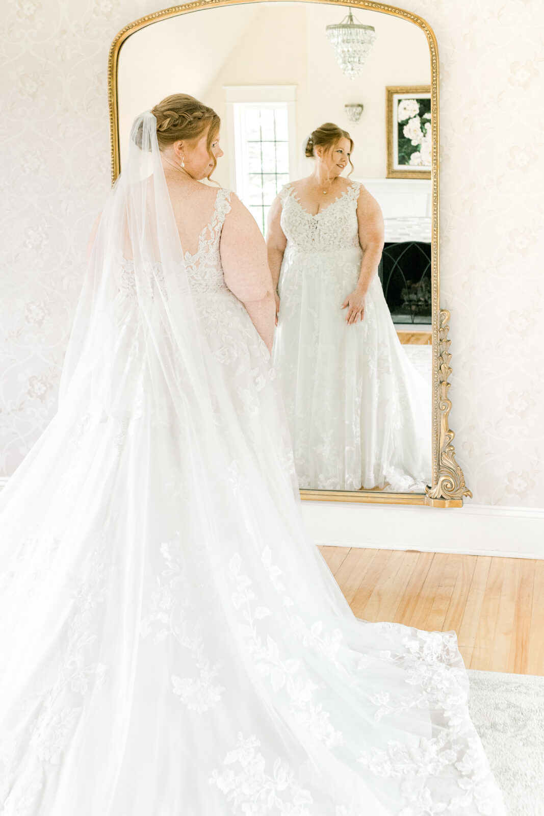 Bride in lace wedding gown with cathedral veil reflected in gold mirror inside the bridal suite at Venue 3Two Grand Rapids Michigan
