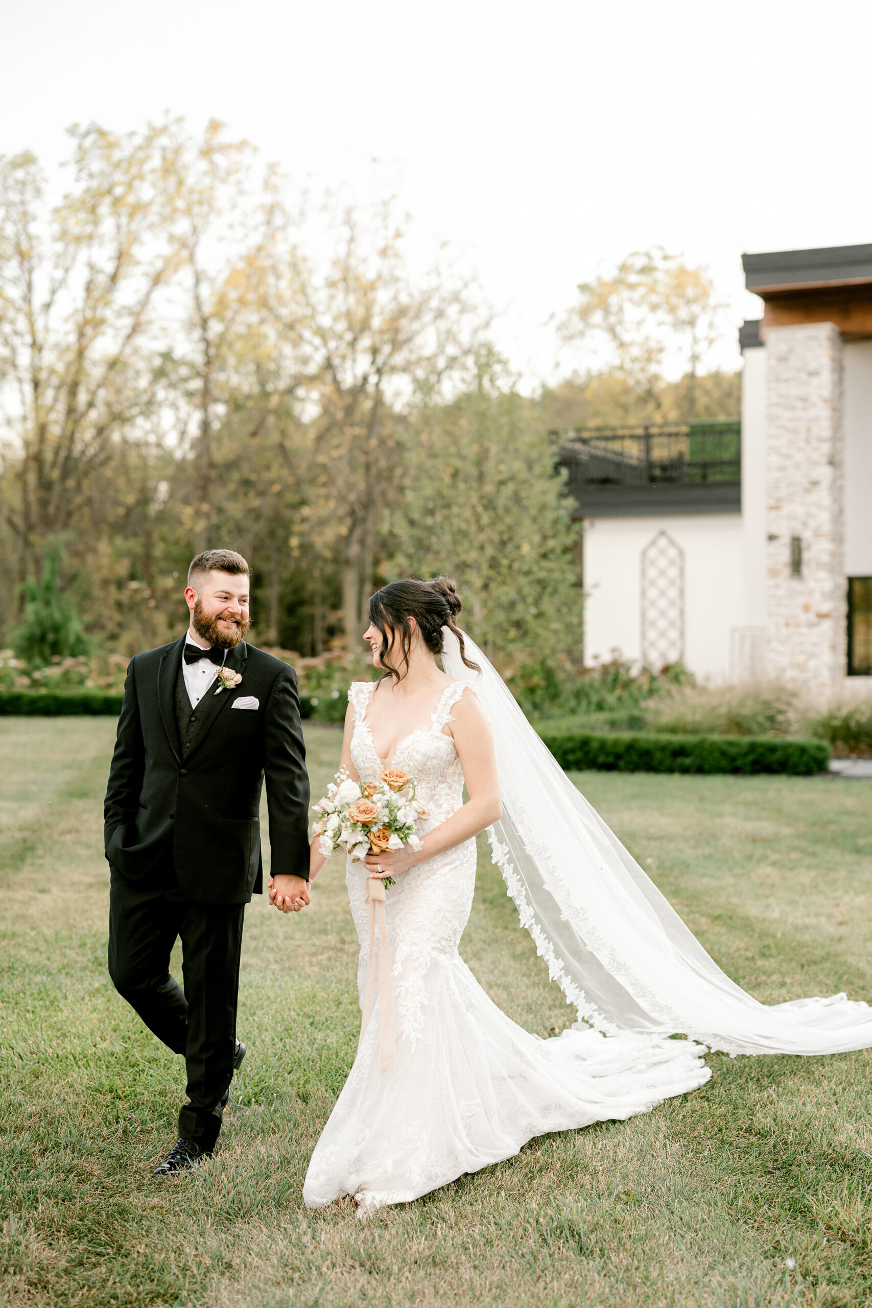 Bride and groom walking hand in hand in front of Hidden Grove Estate at golden hour.