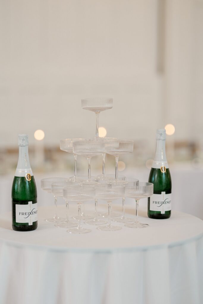 Champagne tower of ribbed coupe glasses with bottles on a white cocktail table at The Broadway Avenue in Grand Rapids