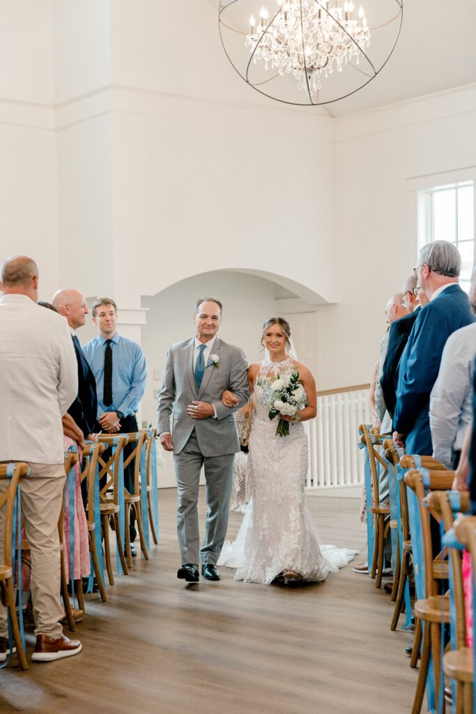 Father of the bride walking his daughter down the aisle under a crystal chandelier at The Broadway Avenue in Grand Rapids