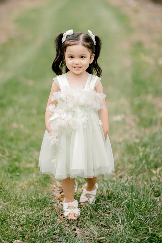 Toddler in a white tulle dress standing in a row of apple trees at Robinette's