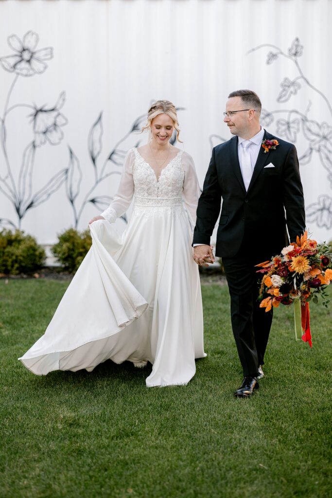 Bride and groom walking in front of the floral mural wall at Ivy House