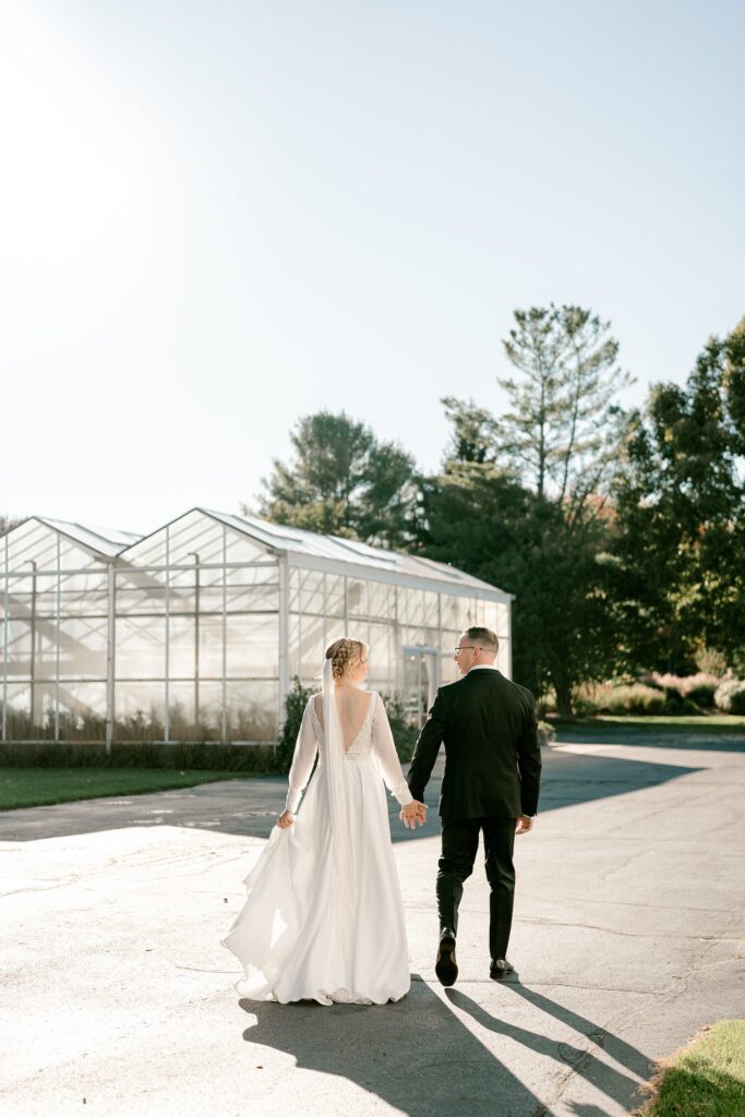Bride and groom walking hand in hand toward the greenhouse
