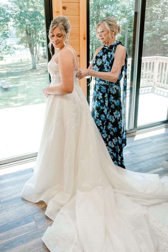 Bride getting ready by the window with a loved one at Waltman Lake Lodge