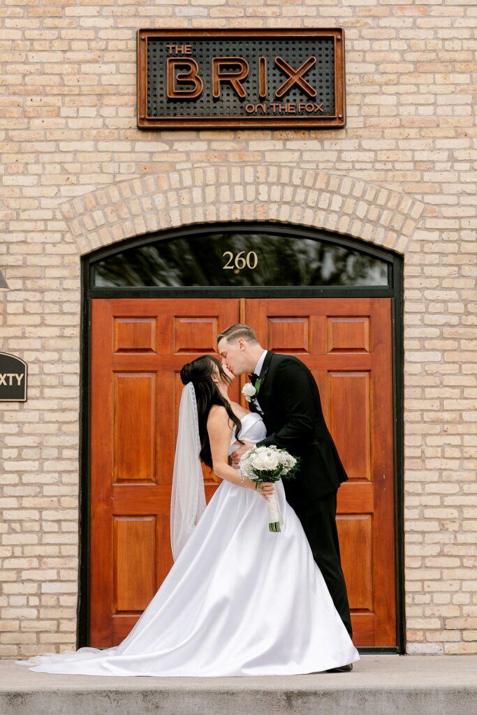 Bride and groom kissing under The BRIX sign at the front doors
