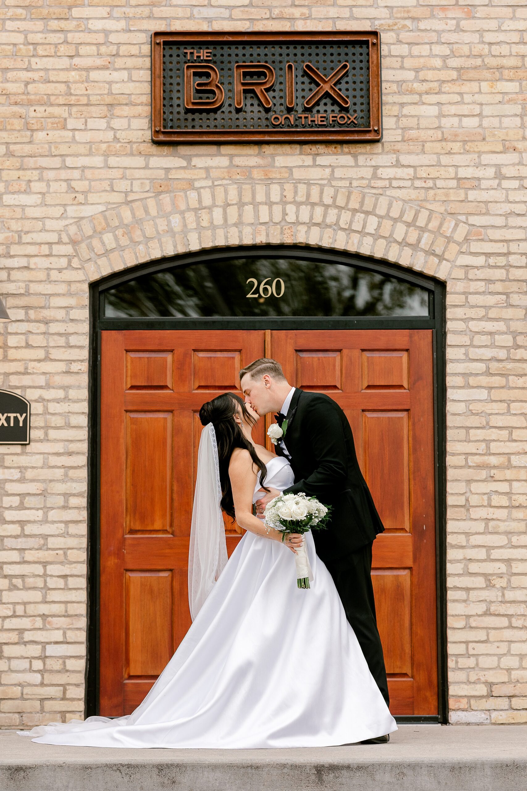 Bride and groom kissing under The BRIX sign at the front doors