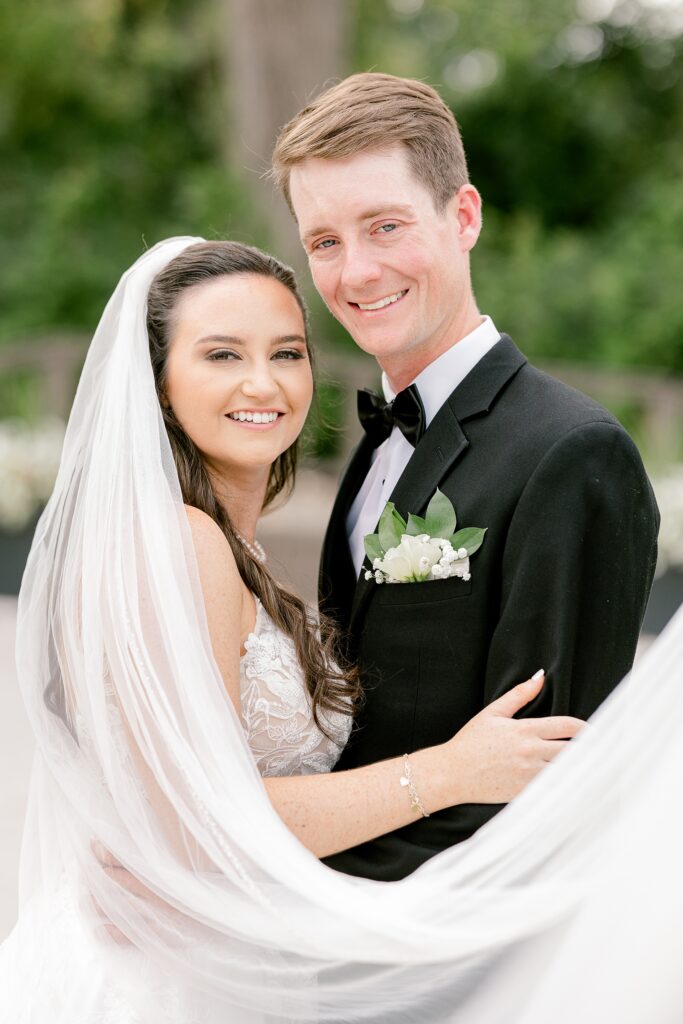 Bride and groom smiling together wrapped in her veil