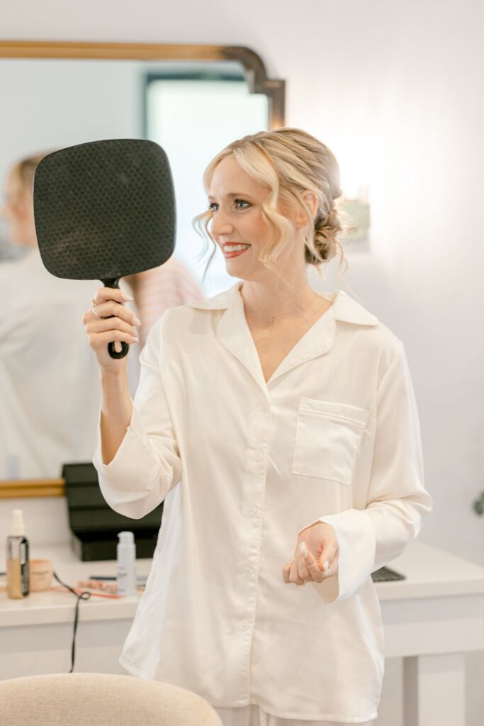 Bride smiling at her hair and makeup in a hand mirror