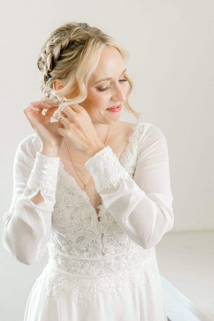 Bride in her lace gown putting on her earrings