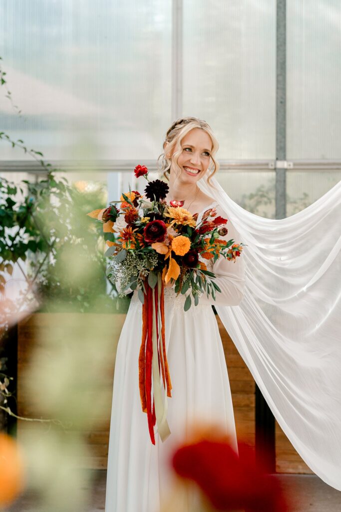 Bride holding a fall bouquet with her veil flowing inside the greenhouse