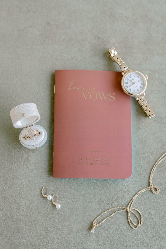 Bride's vow book, ring box, watch and pearl earrings on sage linen