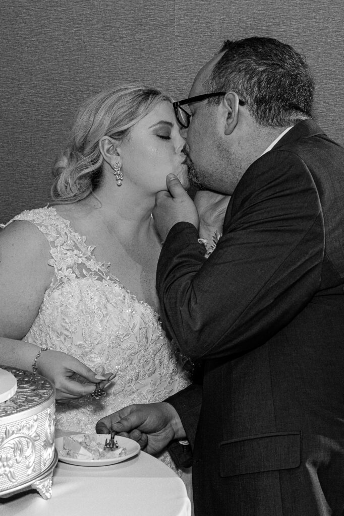 Black and white photo of the couple kissing after cutting the cake