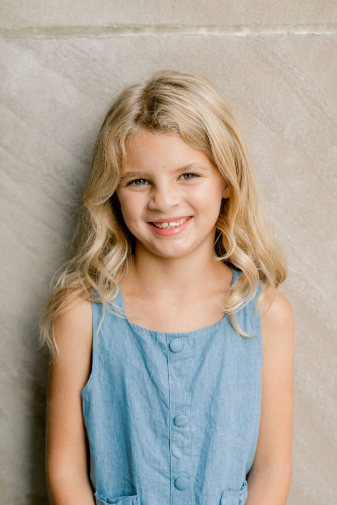 Close-up portrait of a smiling girl with wavy blonde hair against warm limestone in Grand Rapids