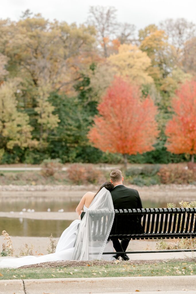 Bride and groom on a bench by the Fox River with fall color