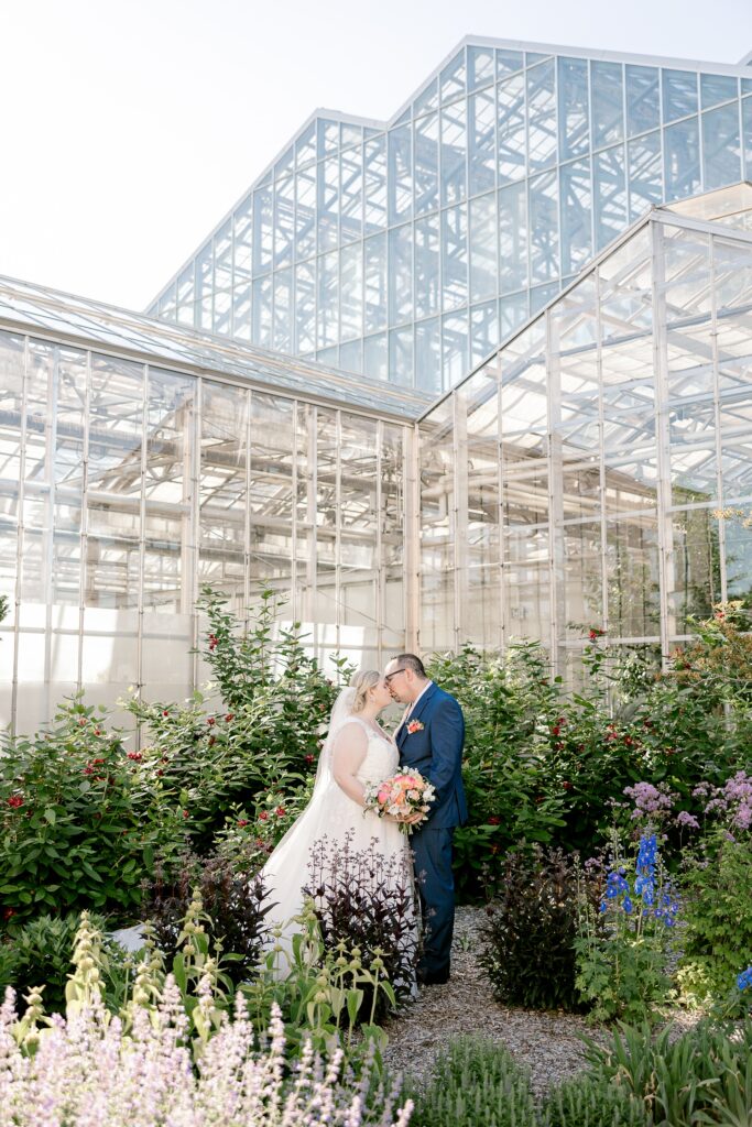 Bride and groom kissing in the gardens in front of the glass conservatory