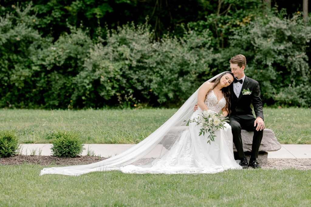 Bride and groom sitting on the lawn with her veil spread out
