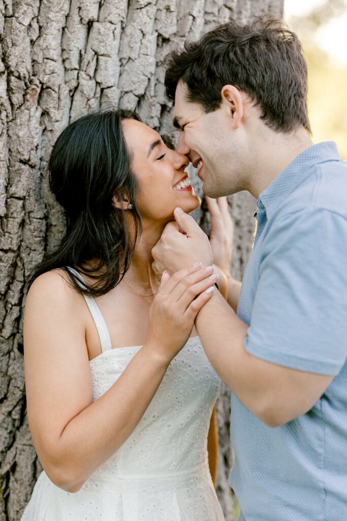 Couple sharing a kiss beside a large tree at Riverside Park during their engagement session