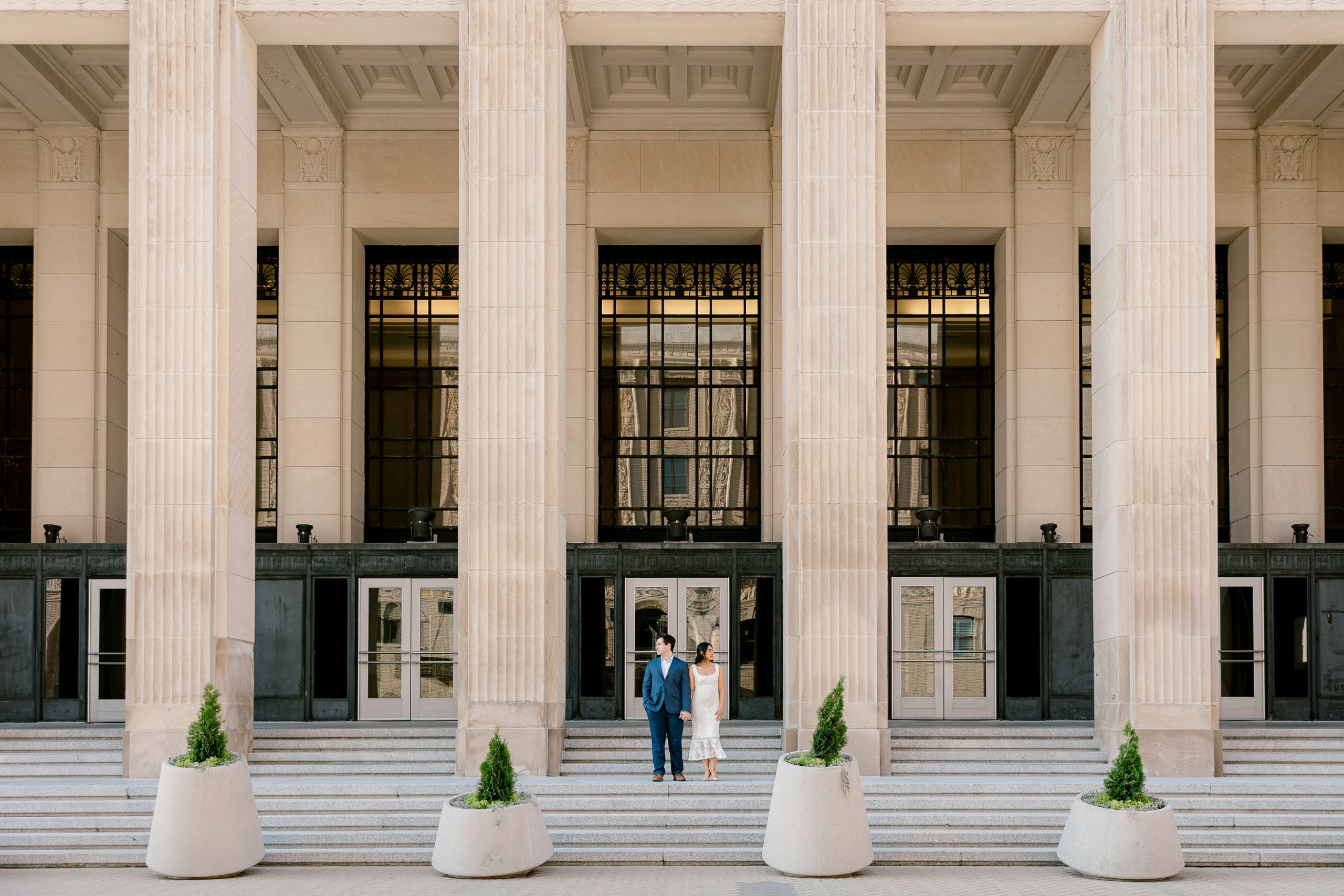 Engaged couple standing on the steps between the tall limestone columns of the Civic Auditorium in downtown Grand Rapids