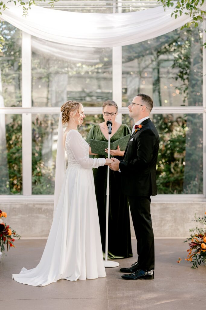 Bride and groom holding hands during their vows in the greenhouse