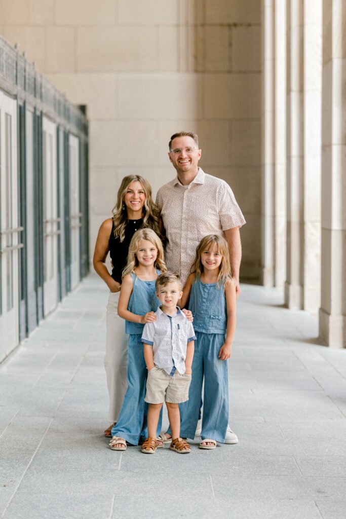 Family in coordinating blue and neutral outfits posing together under the Civic Auditorium columns in Grand Rapids