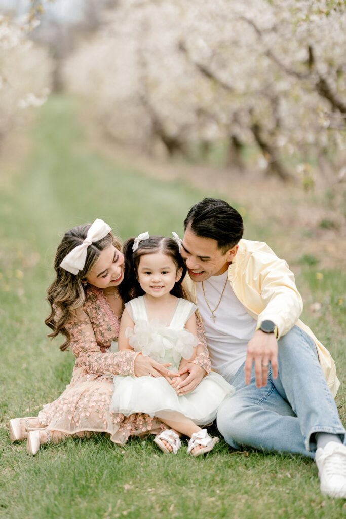 Parents snuggling their little girl while sitting in the apple orchard at Robinette's in Grand Rapids