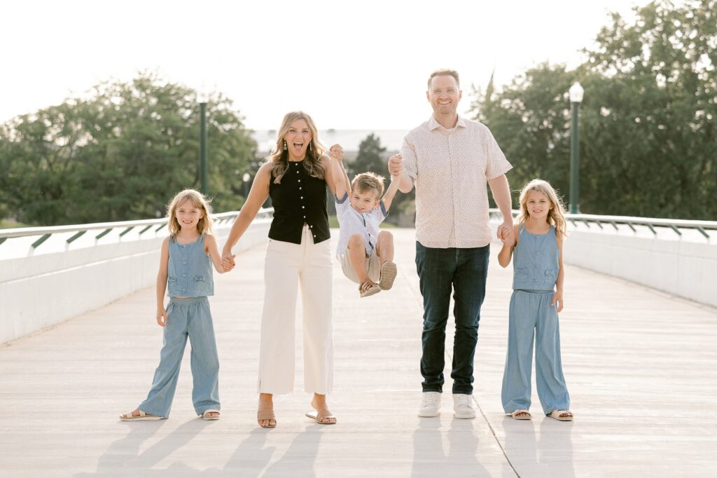 Family holding hands on the Gillett Bridge pedestrian walkway with trees and the downtown Grand Rapids skyline behind them