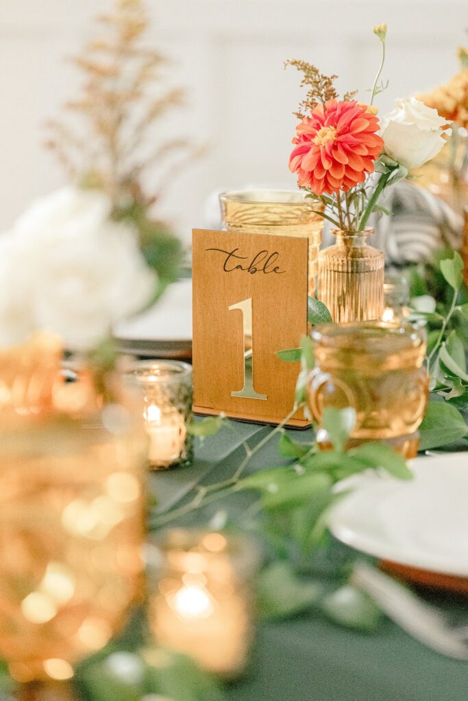 Gold table number with a coral dahlia and votive candles