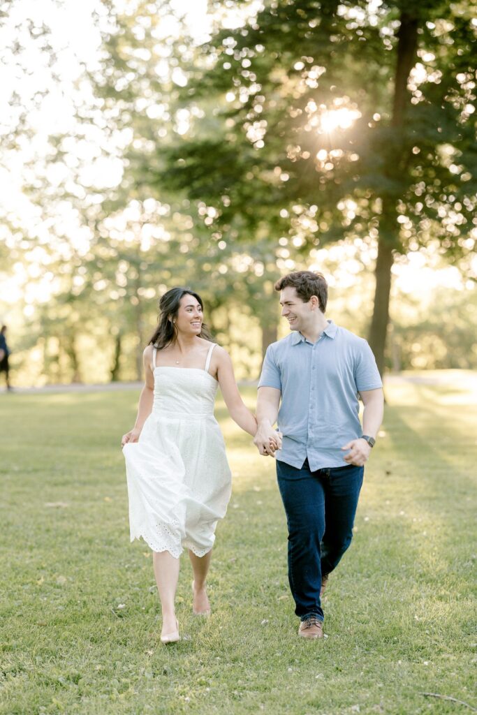Engaged couple walking through the grass at golden hour in Riverside Park, Grand Rapids