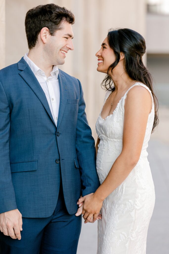 Groom-to-be in a navy suit and his fiancée in a white dress smiling together at DeVos Place