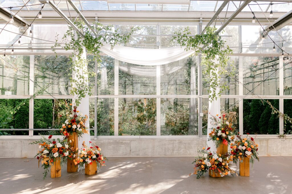 Greenhouse ceremony space at Ivy House with draped fabric, greenery and fall florals