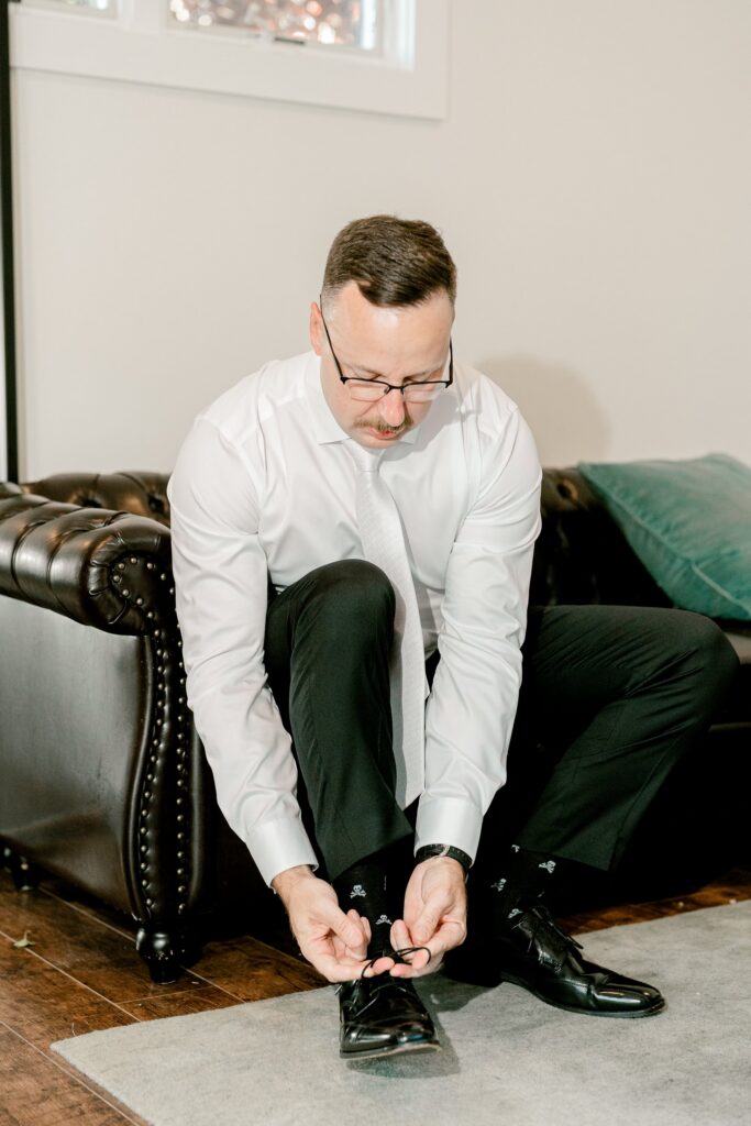 Groom tying his dress shoes in the groom's suite at Ivy House
