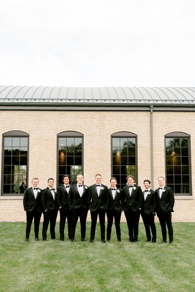 Groom with his groomsmen in black tuxedos on the lawn
