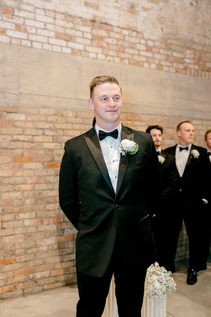 Groom watching his bride walk down the aisle with his groomsmen behind him