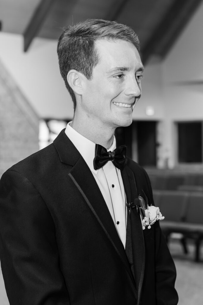 Black and white photo of the groom watching his bride walk down the aisle
