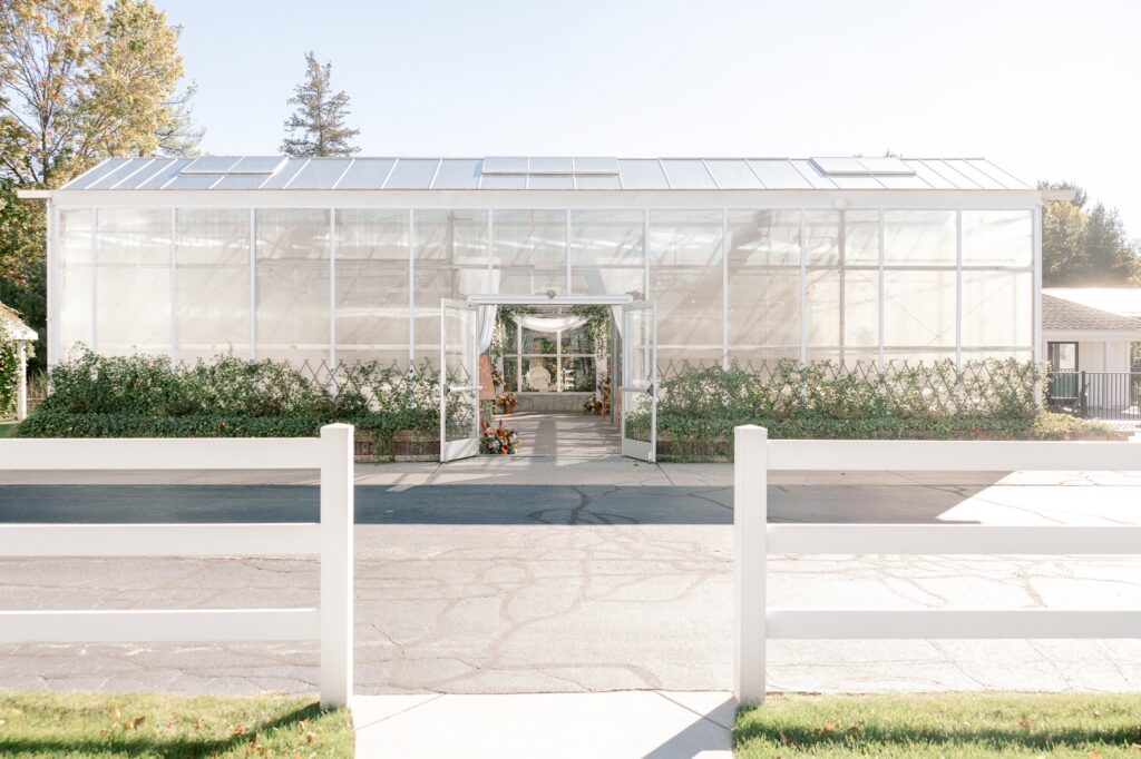 The white greenhouse at Ivy House in Saugatuck behind a white picket fence