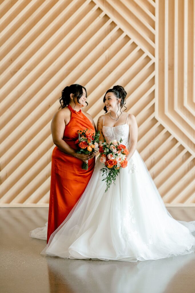 Bride with a bridesmaid in a burnt orange dress in front of the wood slat wall at Leona Road