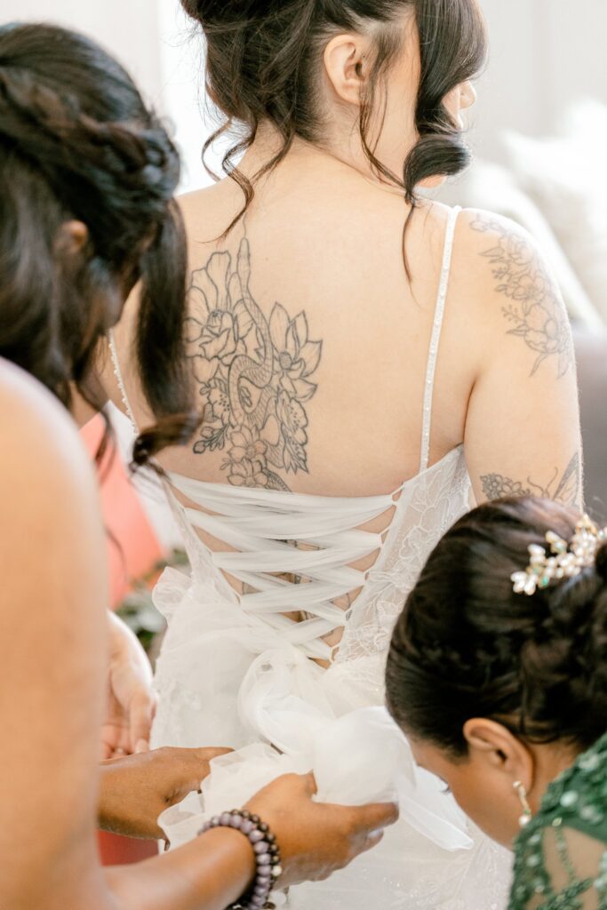 Bridesmaids lacing up the back of the bride's wedding gown at Leona Road