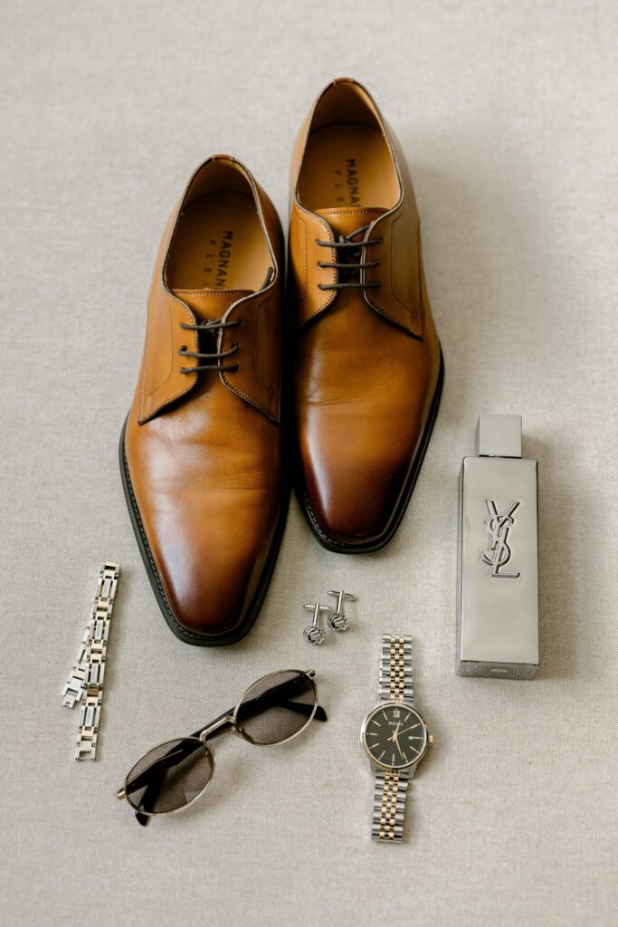 Groom details with brown dress shoes, watch, sunglasses and cologne at the Amway Grand Plaza before his Leona Road wedding