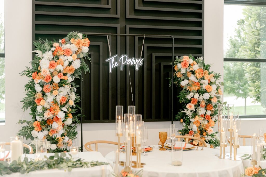 Sweetheart table with orange floral installations and a black slat backdrop at Leona Road