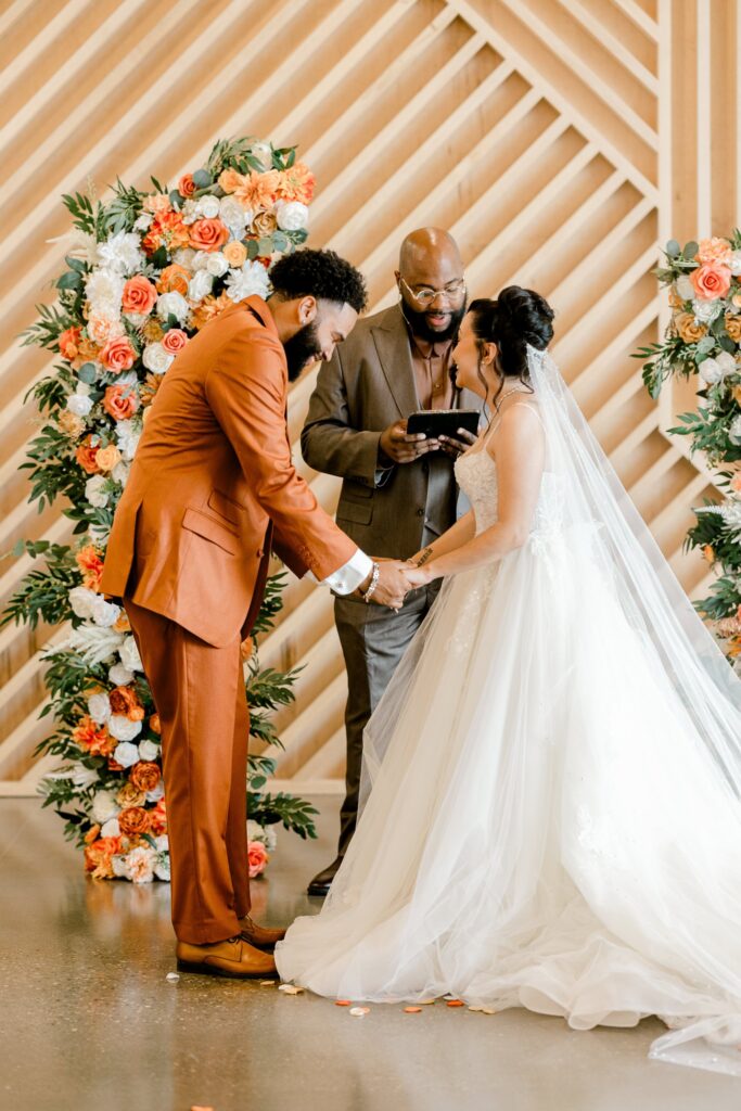 Bride and groom at the floral-framed wood slat wall during their Leona Road wedding ceremony