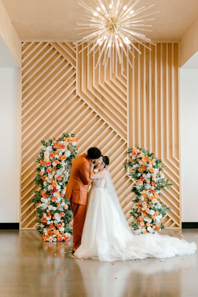 First kiss in front of the wood slat wall and orange florals at Leona Road