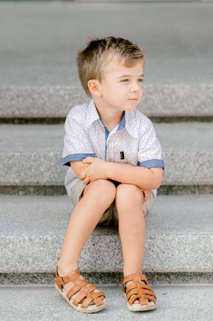 Little boy sitting on the stone steps hugging his knees during a downtown Grand Rapids family session
