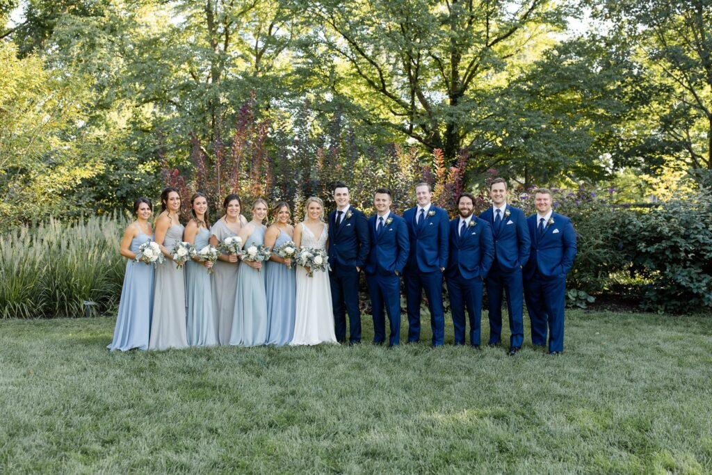 Wedding party in navy suits and dusty blue dresses in the gardens at The Morton Arboretum in Lisle, Illinois