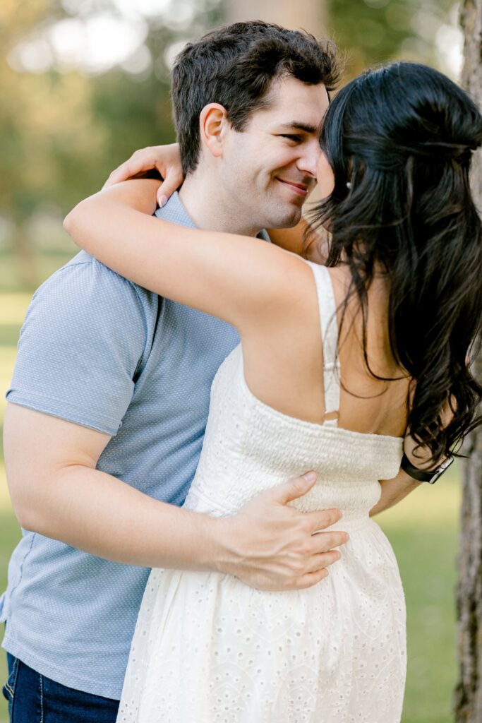 Engaged couple laughing together beside a big tree trunk at Riverside Park in West Michigan