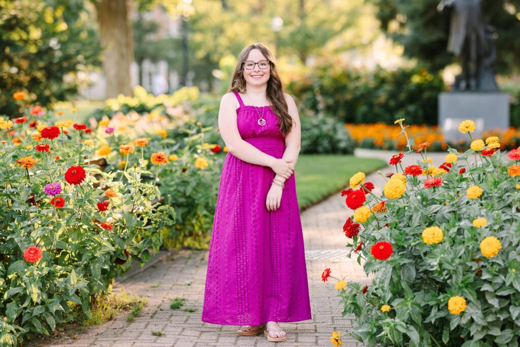 Senior girl in a pink dress walking through colorful flower gardens in downtown Holland, Michigan